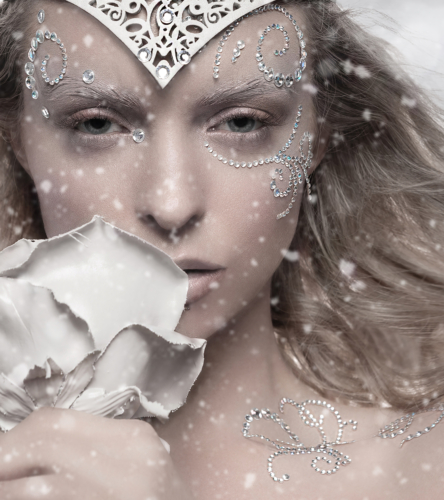 Beautiful Caucasian girl wearing crown with white make up in a snow storm with a white rose