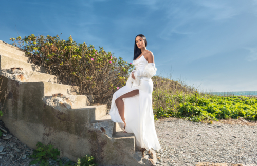 interracial woman  wearing white wedding dress on stairs at the beach 